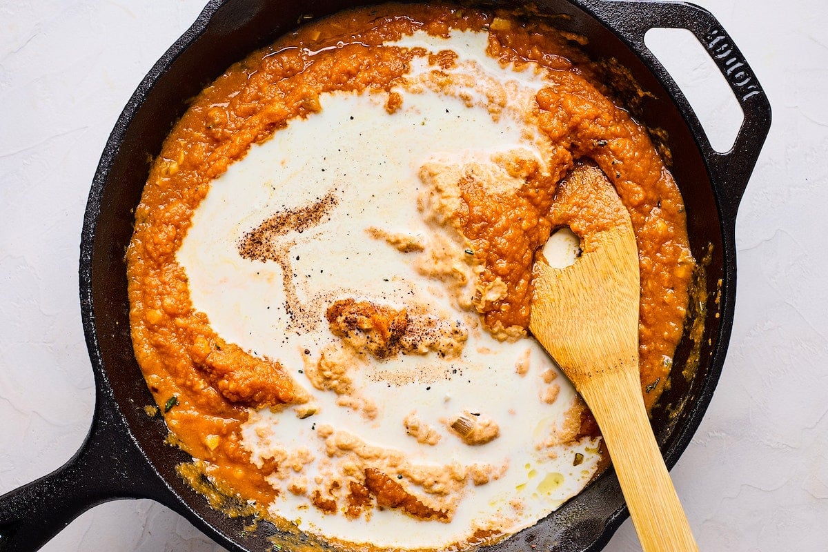 pumpkin pasta sauce with heavy cream in cast iron skillet with wooden spoon.