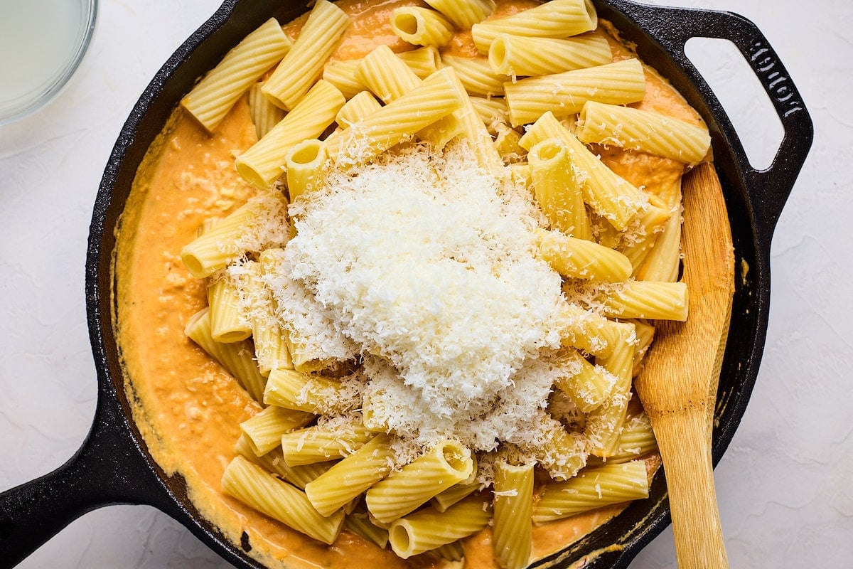 pumpkin pasta in cast iron skillet with Parmesan cheese with wooden spoon.