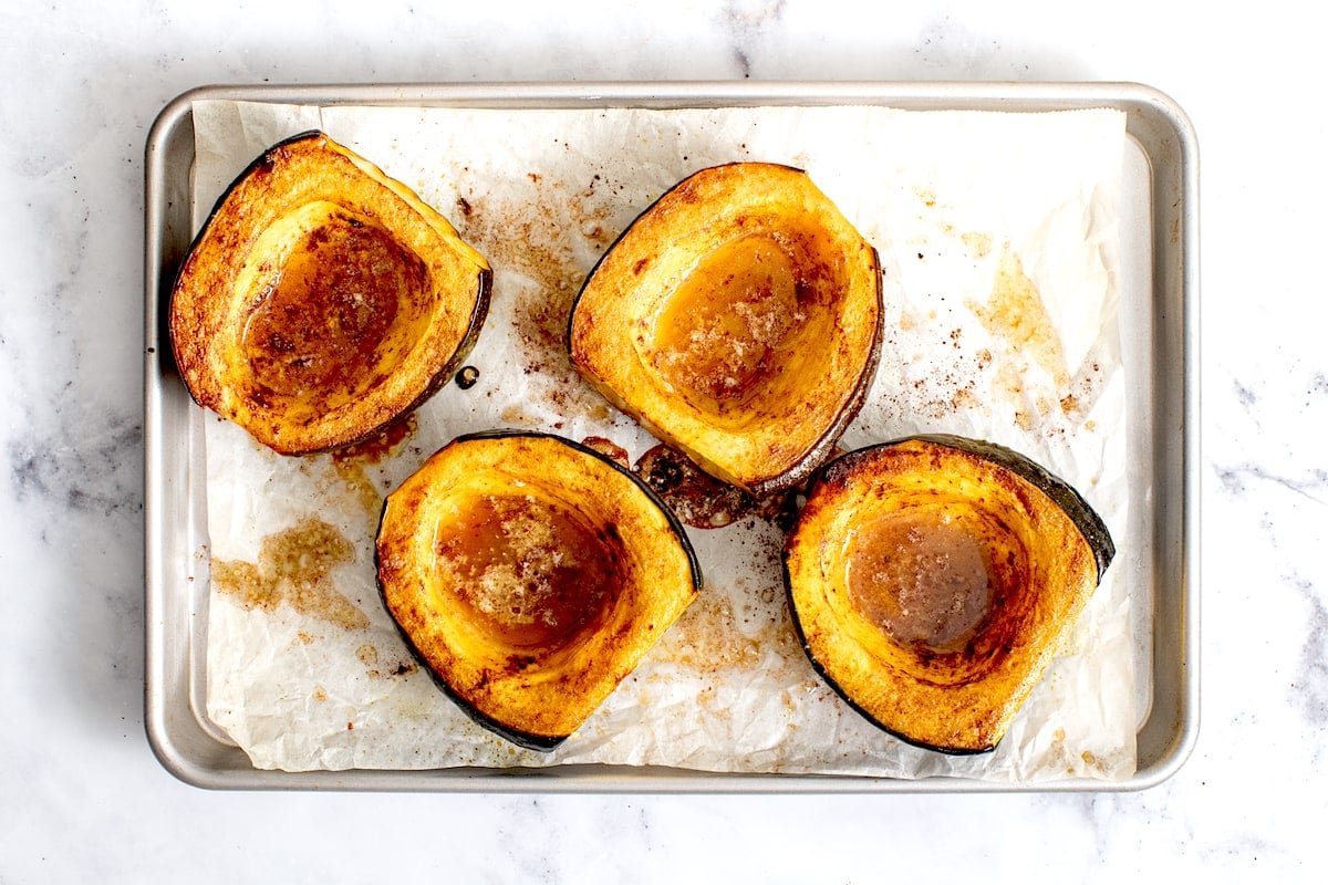 roasted acorn squash on baking sheet with butter, maple syrup, and cinnamon.
