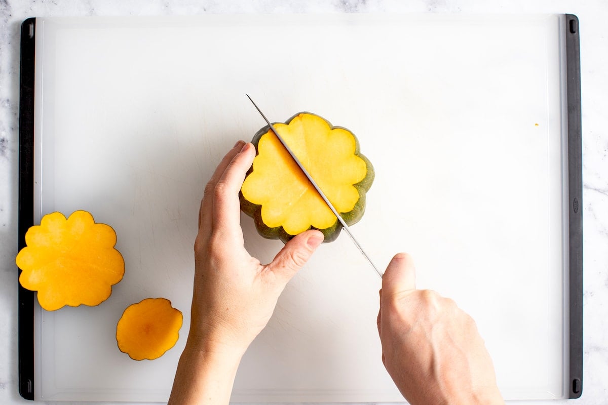 cutting acorn squash in half with knife on cutting board.