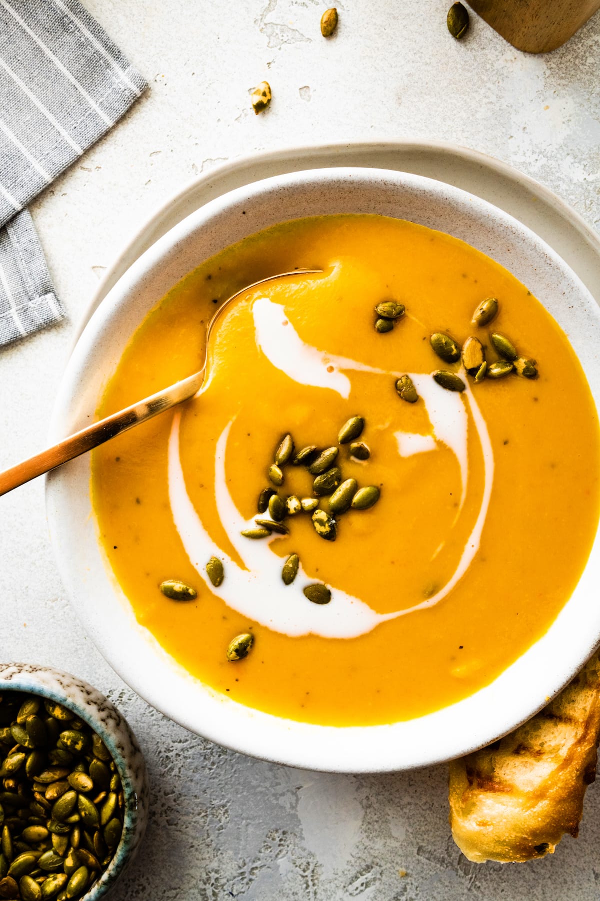 butternut squash pear ginger soup in bowl with coconut milk, pepitas, and a spoon.