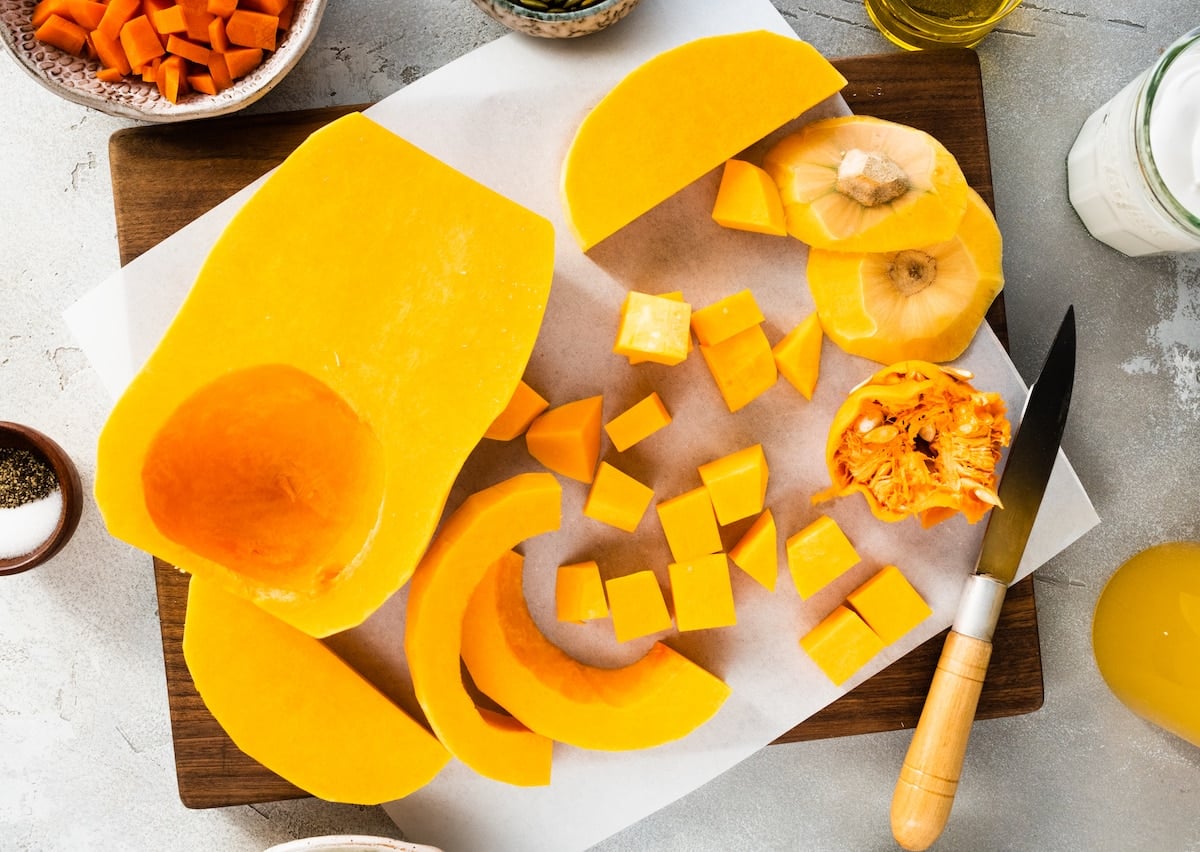 butternut squash being cut into cubes on wood cutting board.