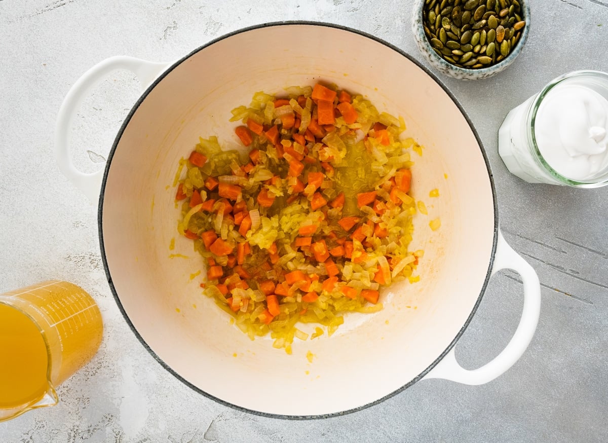 onion, carrots, and garlic being sautéed in white pot to make butternut squash soup.