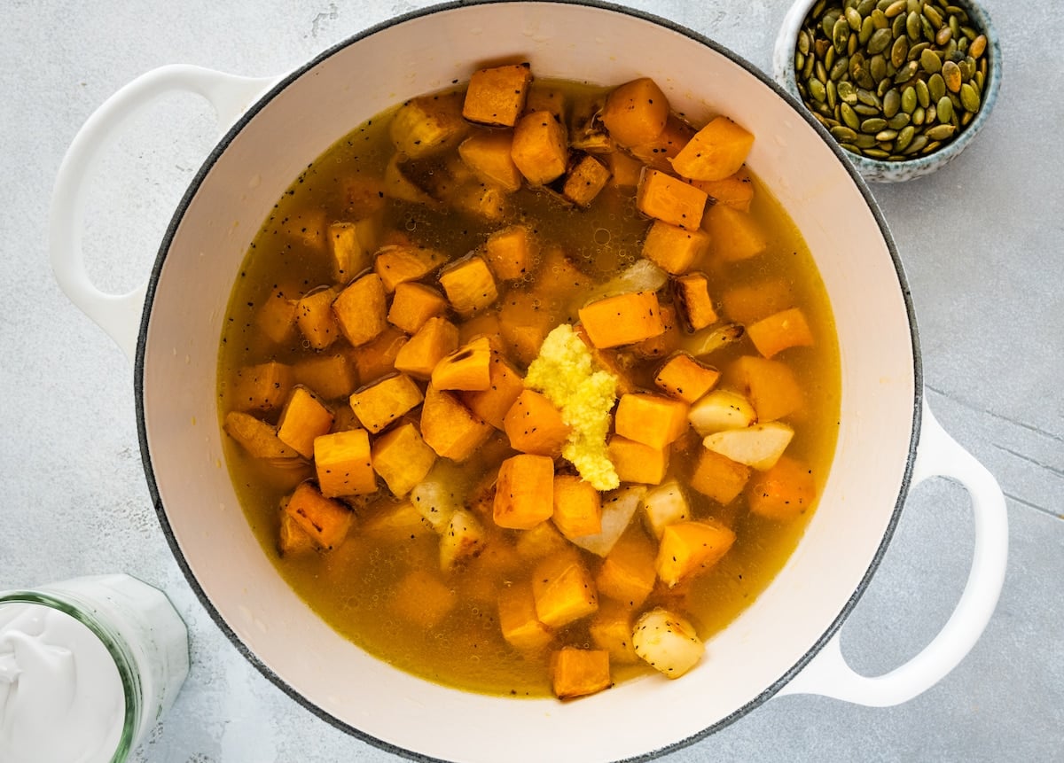 roasted butternut squash, pears, ginger, and vegetable broth in white pot.