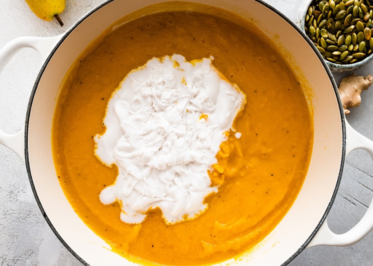 coconut milk being added to roasted butternut squash pear ginger soup in pot.