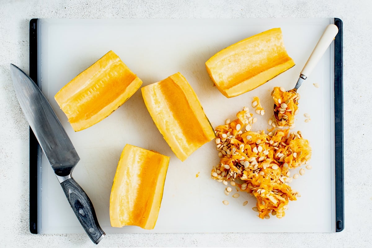 delicata squash cut in half with seeds scraped out on cutting board with knife.