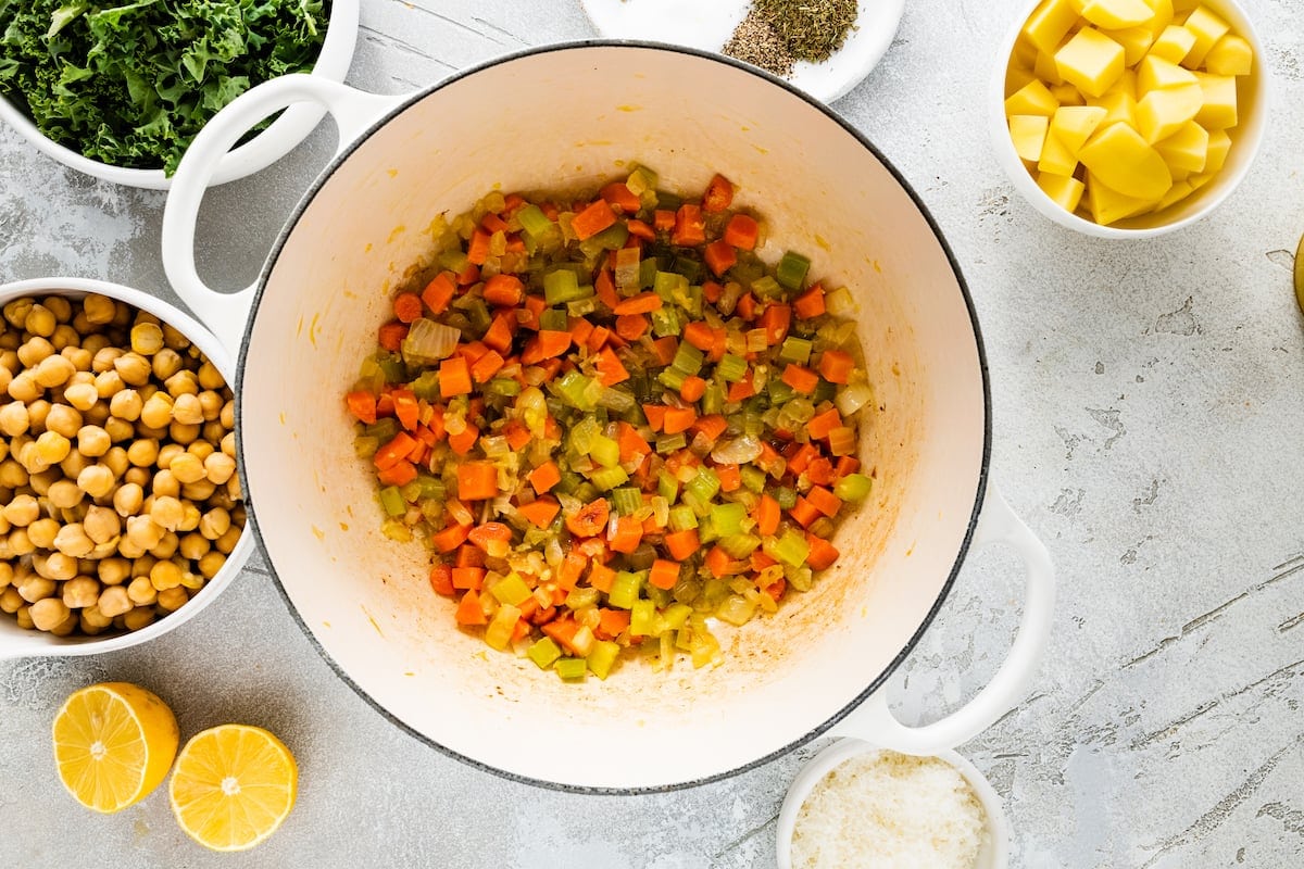 carrot, celery, onion, and garlic cooking in large white soup pot.