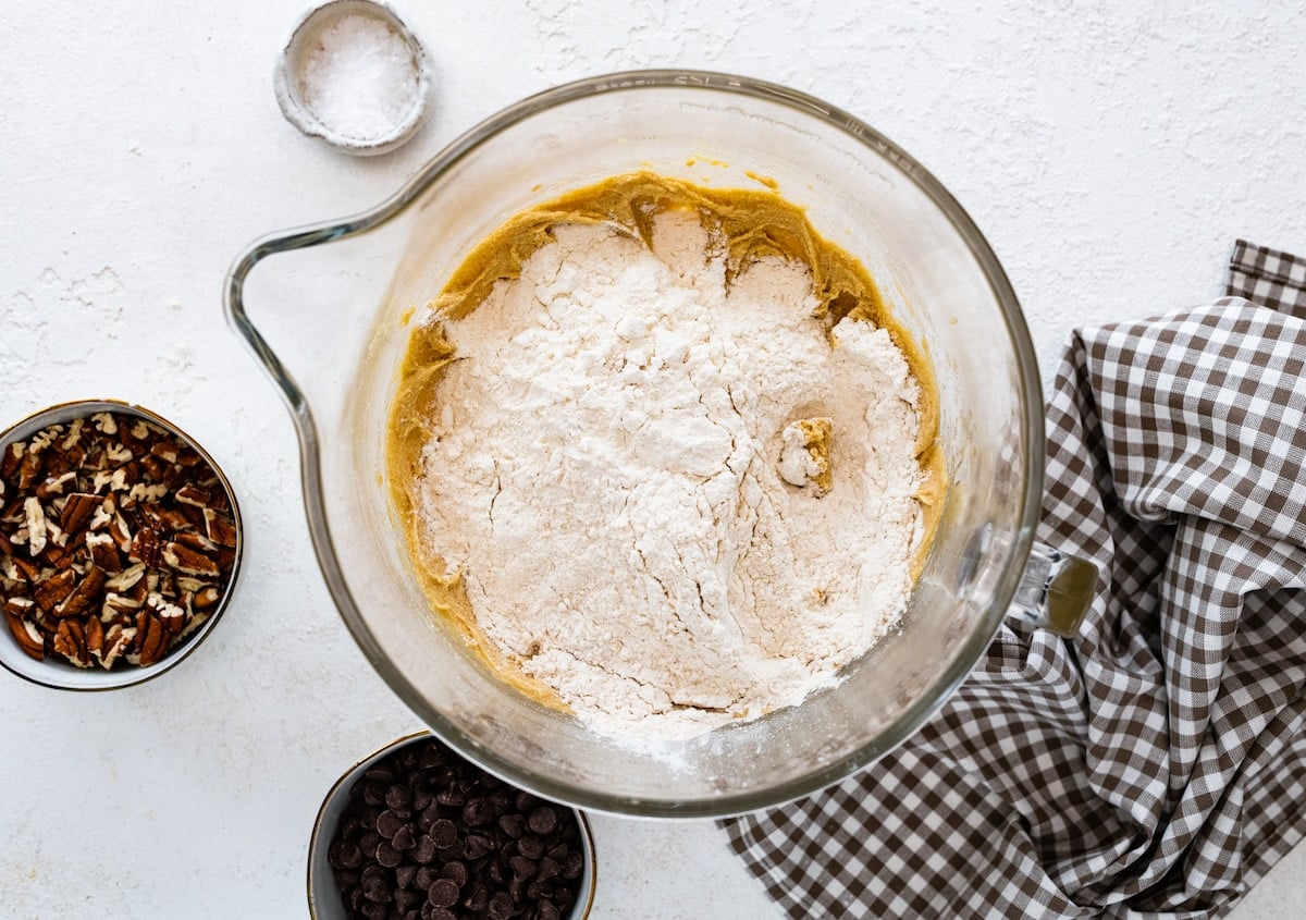 adding flour to cookie dough in glass mixing bowl.