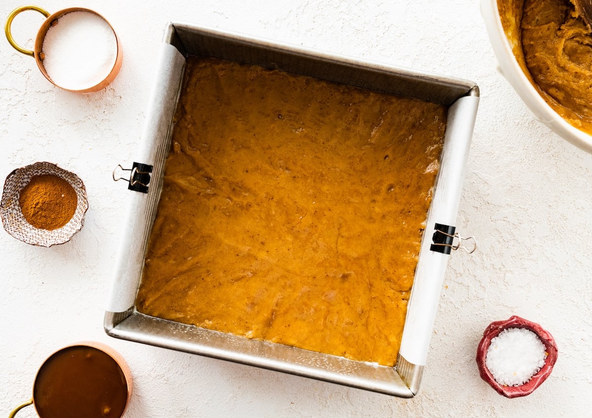 snickerdoodle blondie batter being pressed into a baking pan that is lined with parchment paper.