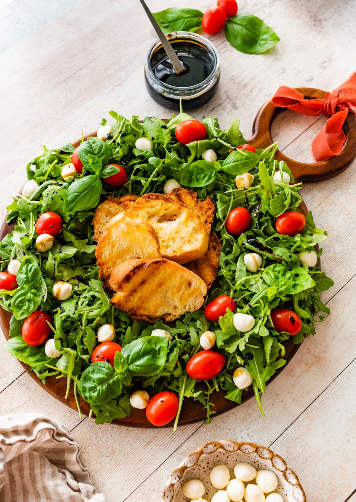 caprese wreath salad on wood board with toasted bread.