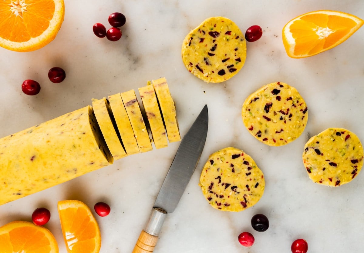 slicing cranberry orange pistachio shortbread cookies into slices with knife.