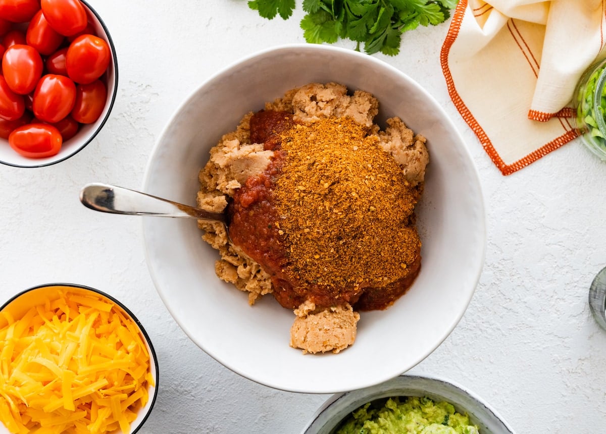 refried beans with salsa and taco seasoning in bowl with spoon.