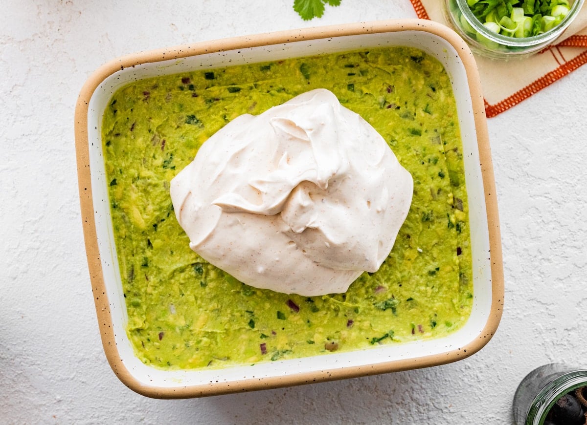 adding sour cream to 7 layer dip in dish.
