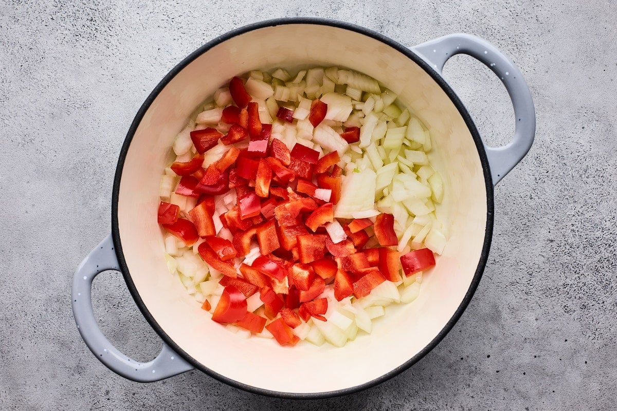 onion and red bell pepper cooking in large pot to make goulash.