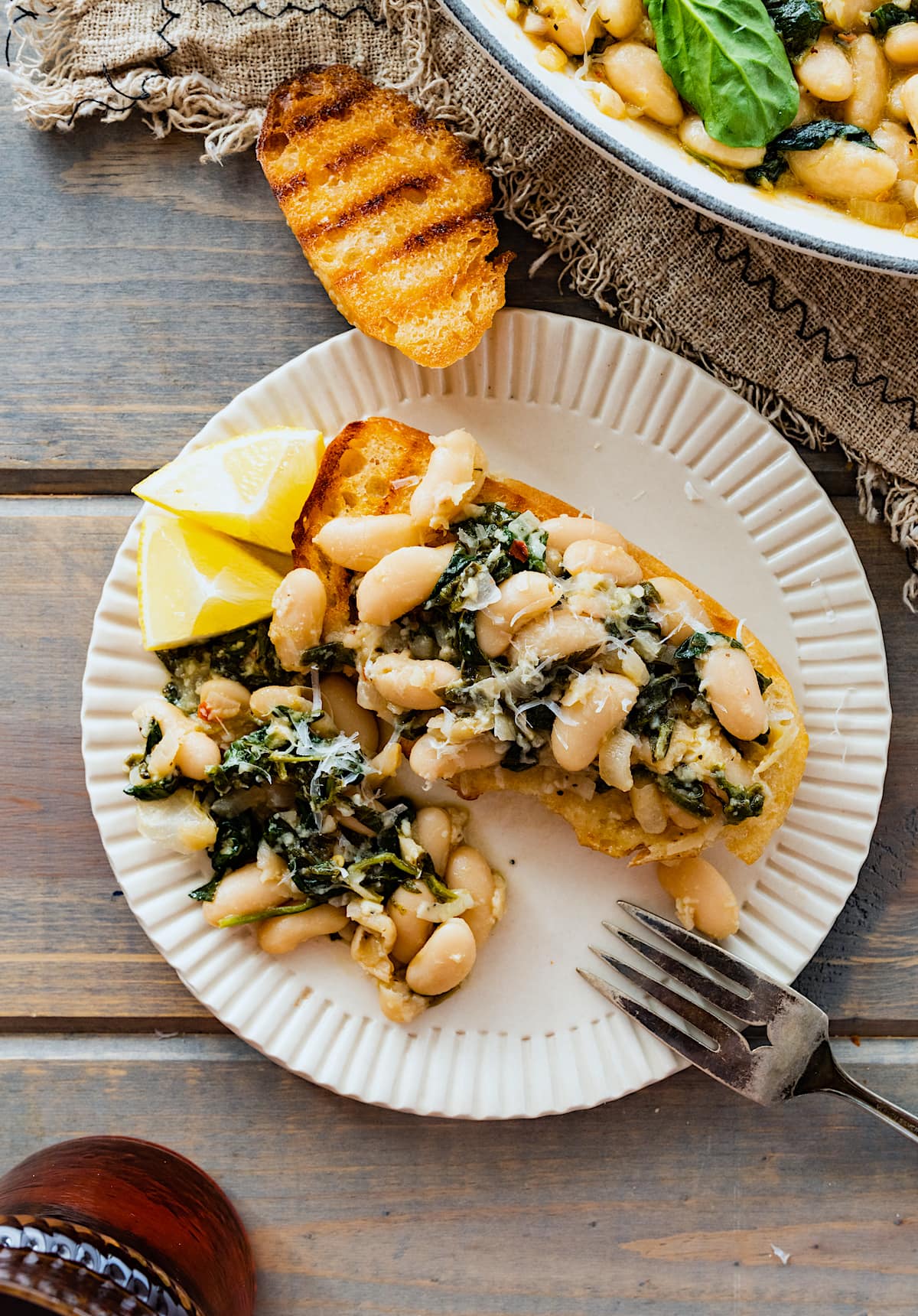 creamy white beans with spinach on toast with Parmesan cheese on plate with fork.