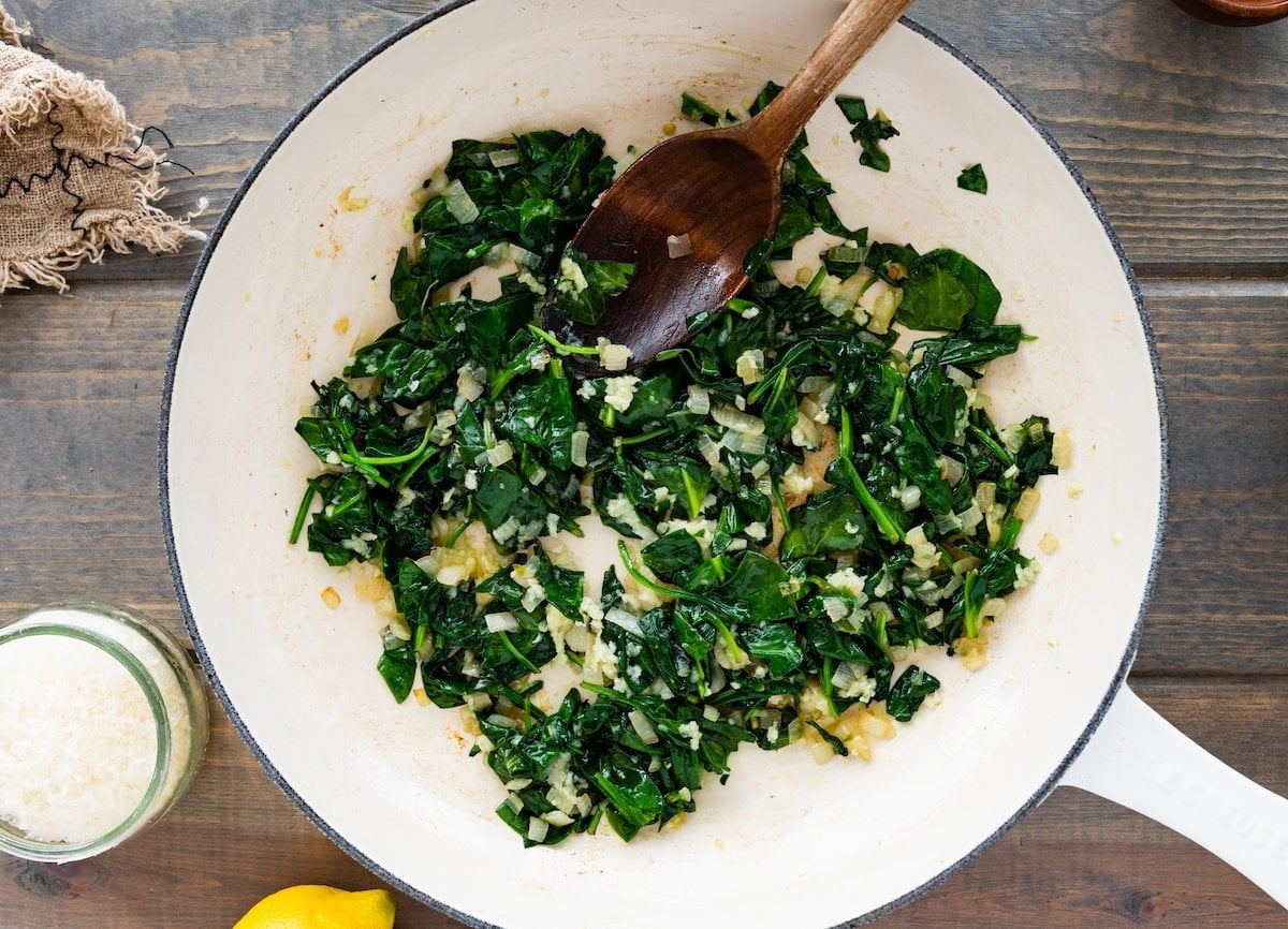 sautéed spinach in skillet with wooden spoon.