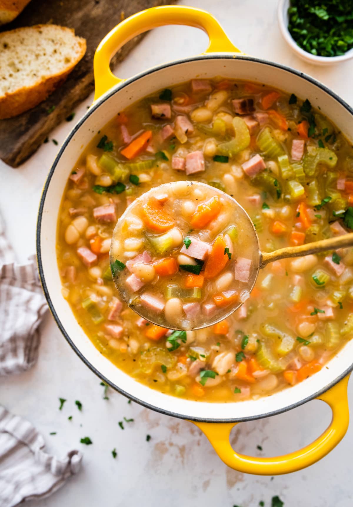 a ladle serving ham and bean soup from a large yellow pot.