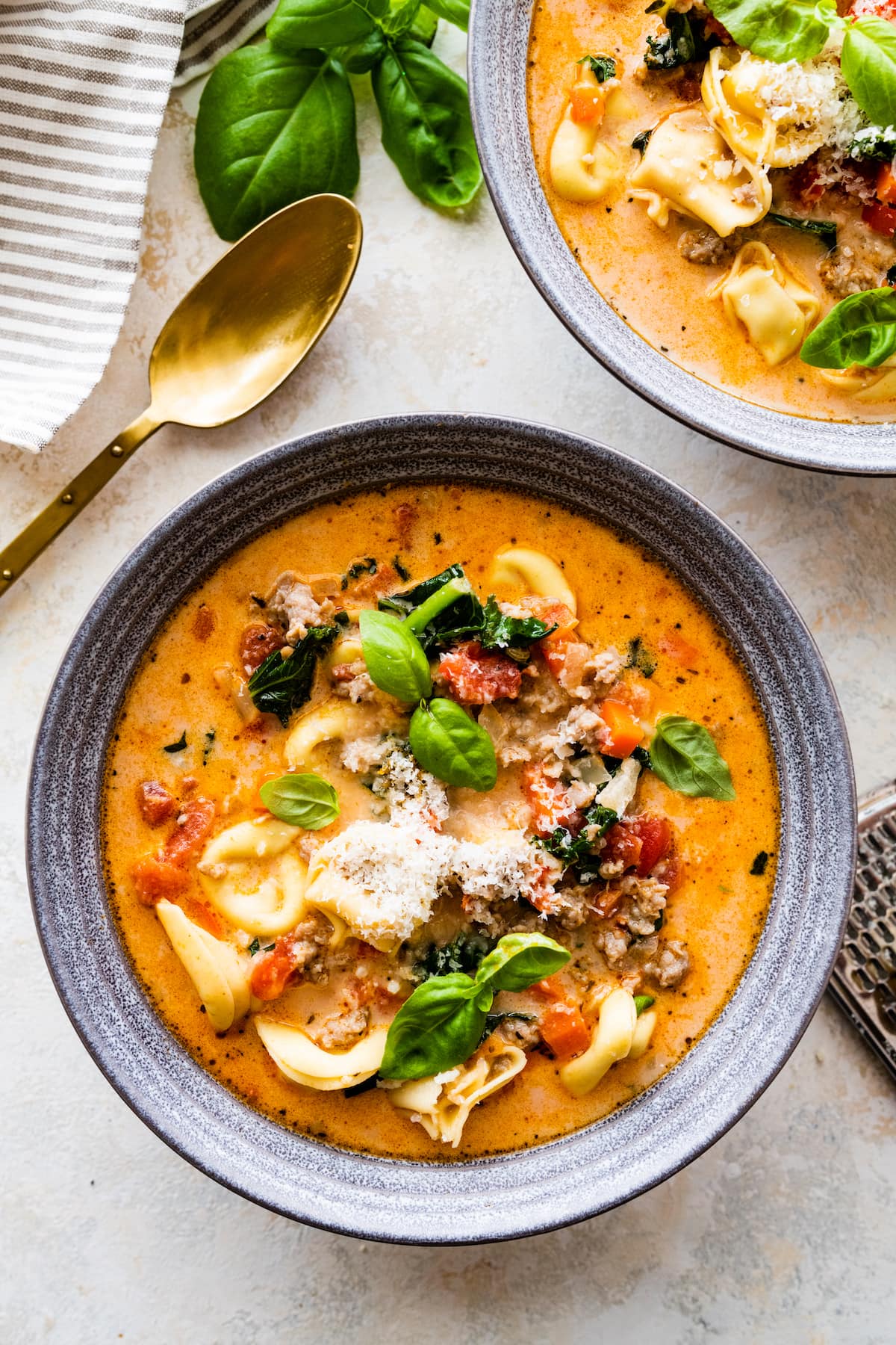 creamy Italian sausage tortellini soup in bowl with basil and Parmesan cheese.