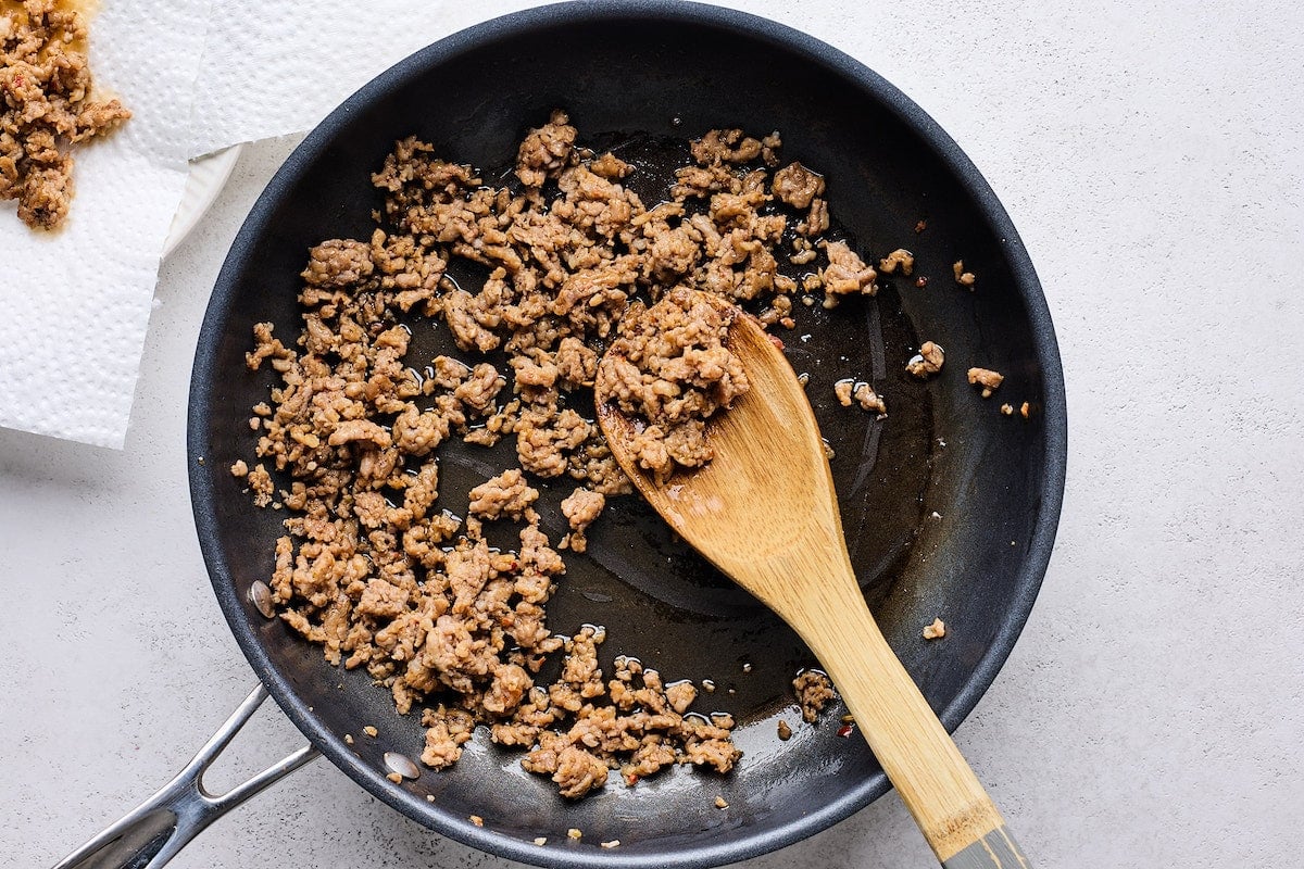 Italian sausage cooking in skillet with wooden spoon.