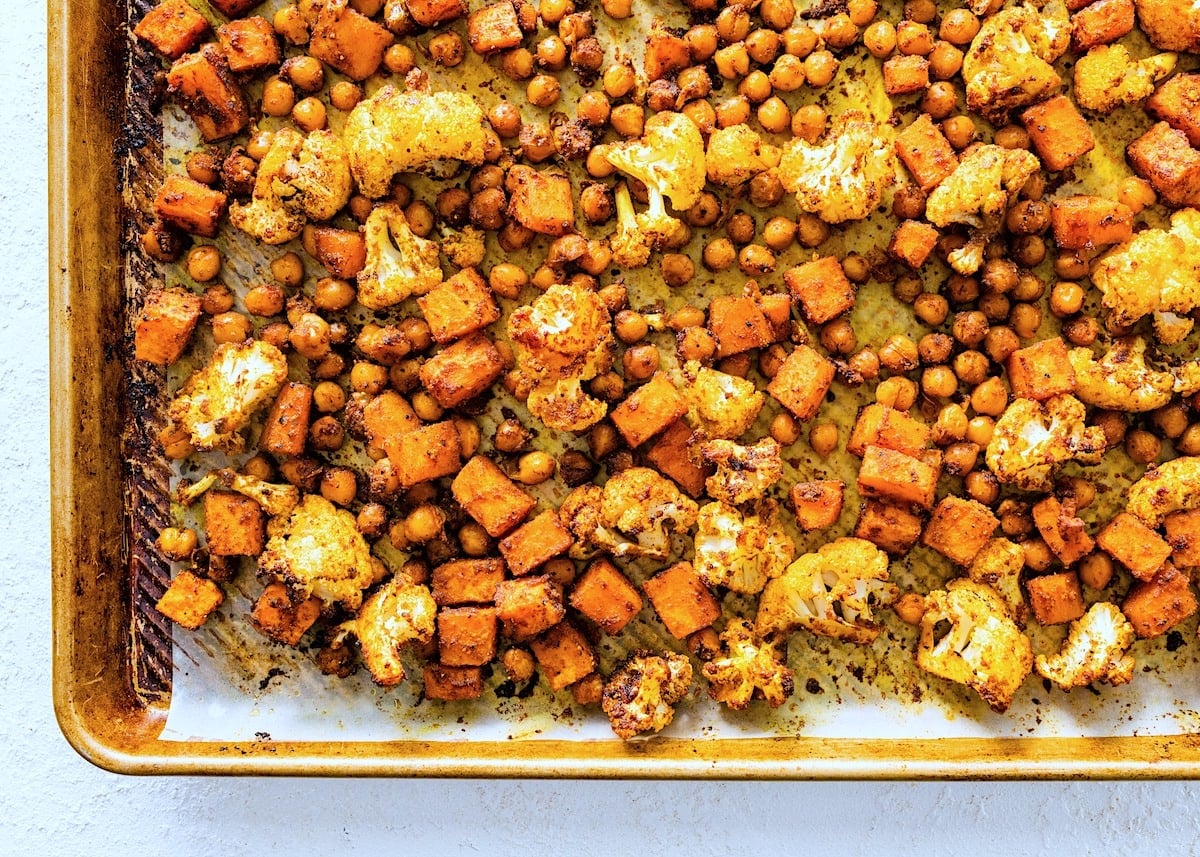 roasted cauliflower, sweet potatoes, chickpeas, and spices on baking sheet.