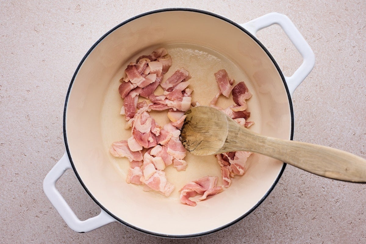 bacon cooking in white pot with wooden spoon to make zuppa toscana.