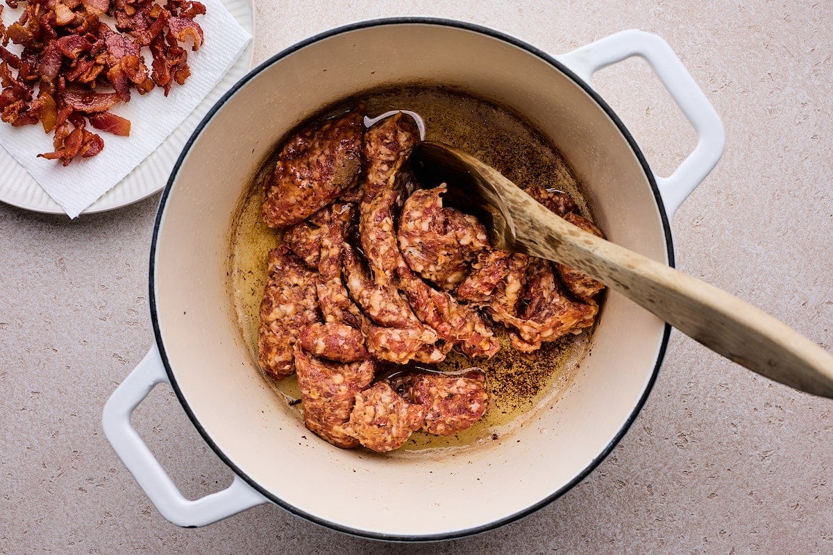 Italian sausage cooking in white pot with wooden spoon.