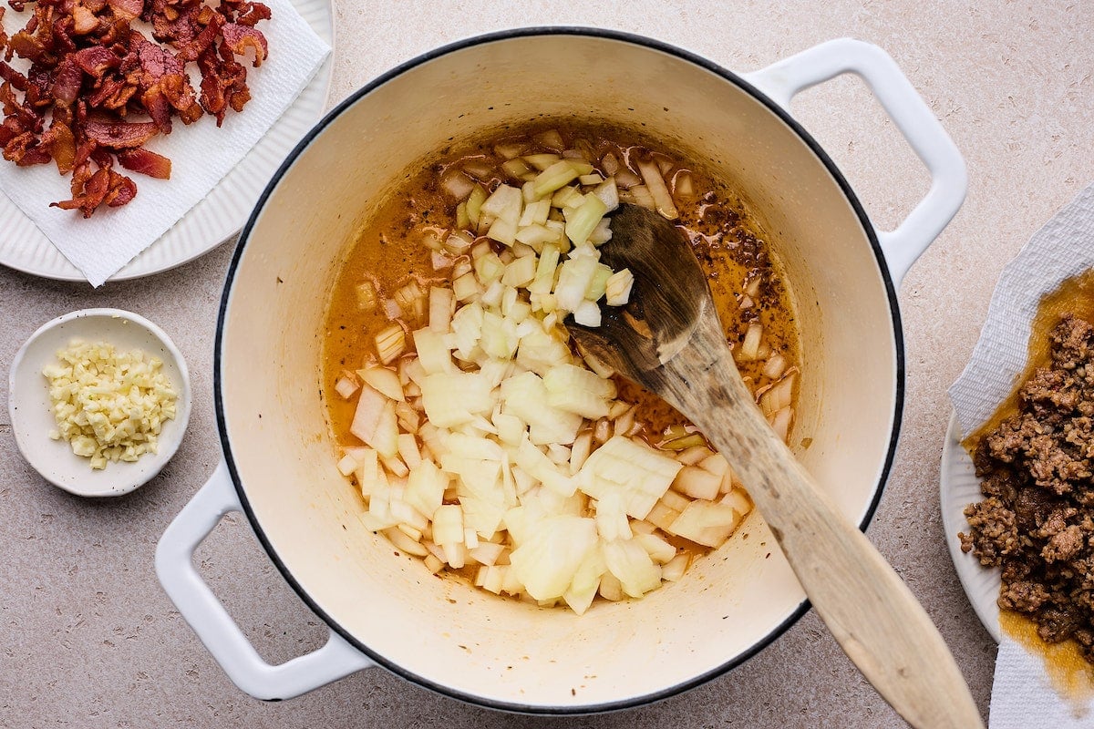 onion cooking in large white pot with wooden spoon to make zuppa toscana.