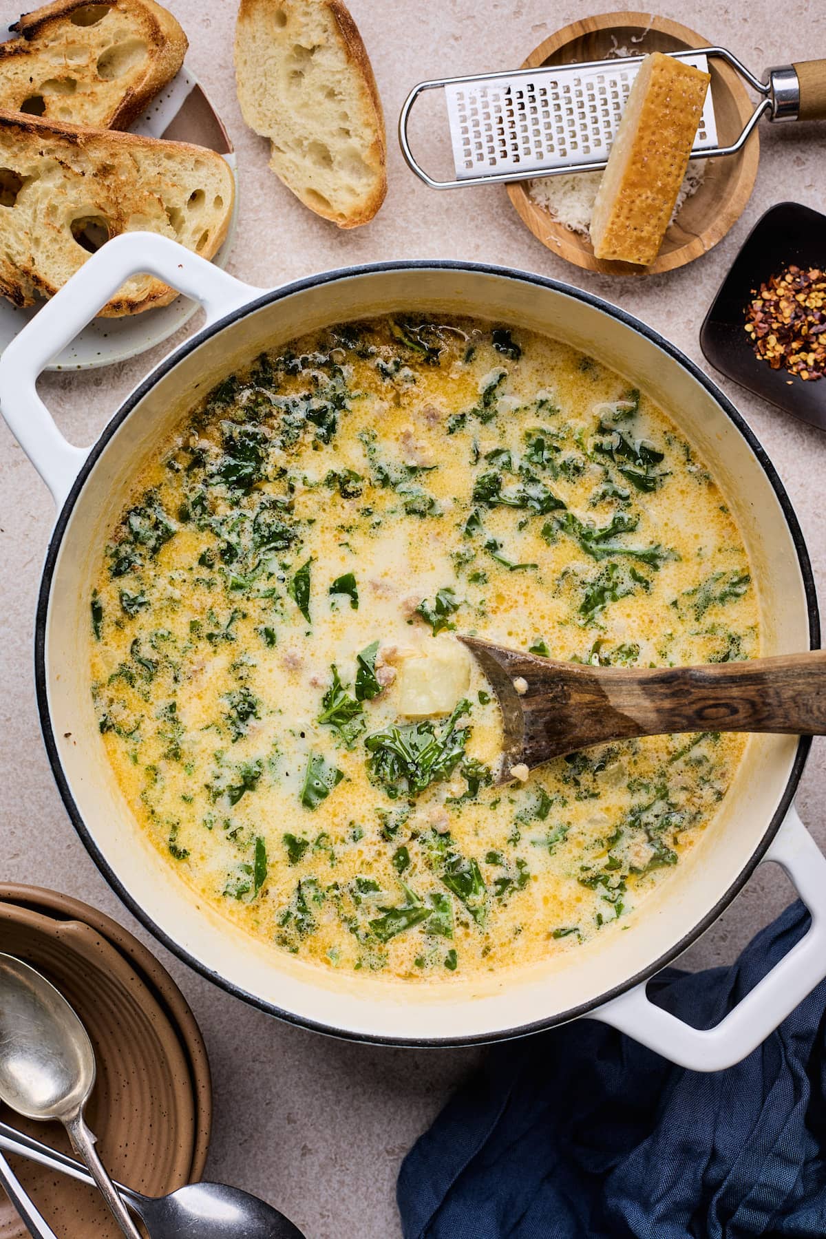zuppa toscana soup in large white pot with wooden spoon.