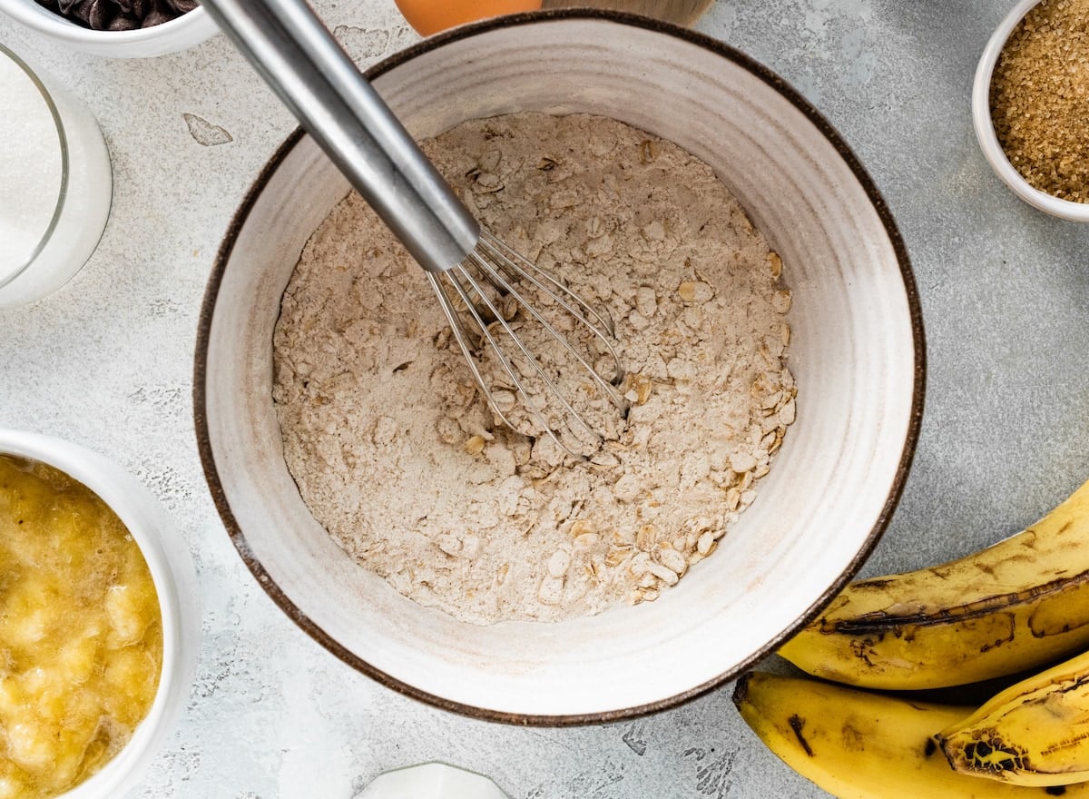 dry ingredients and oats in mixing bowl with whisk to make banana oatmeal muffins.