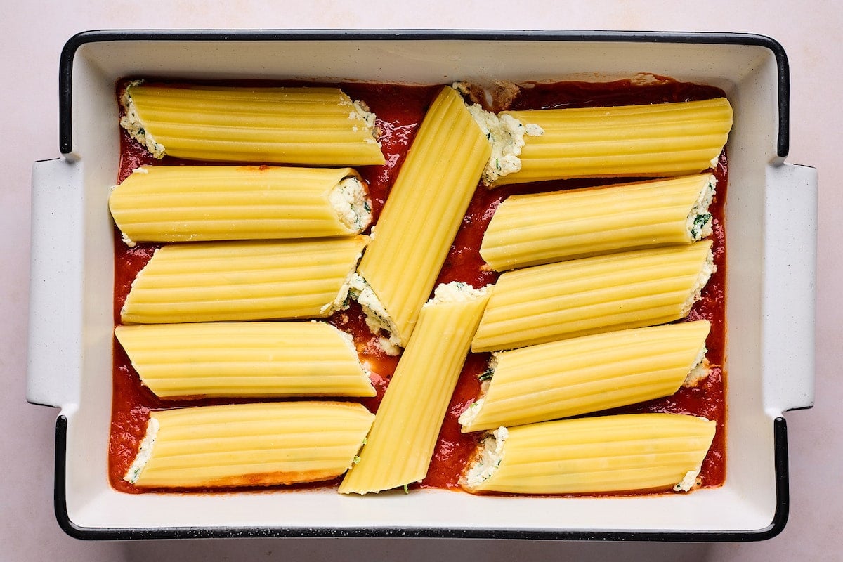 manicotti stuffed with cheese filling in baking dish with marinara sauce.