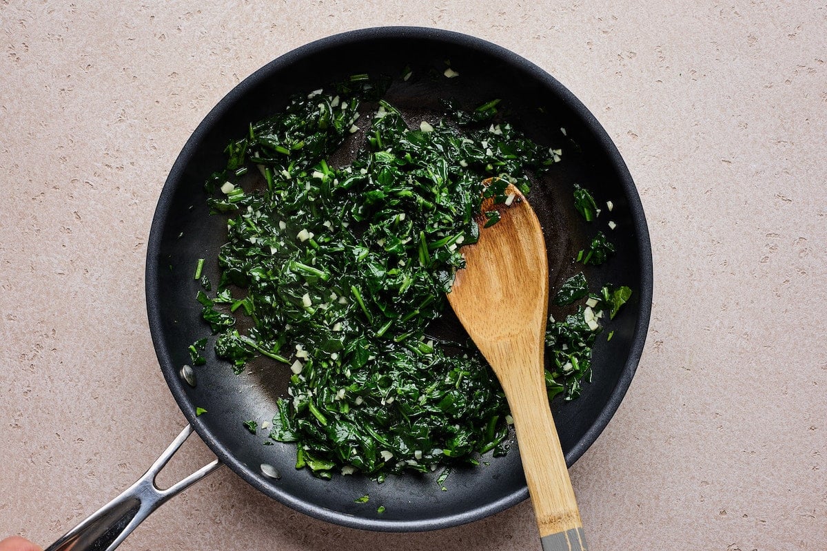 sautéed spinach with garlic in skillet with wooden spoon.