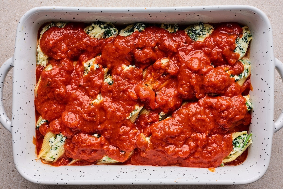 stuffed shells topped with marinara sauce in baking dish.