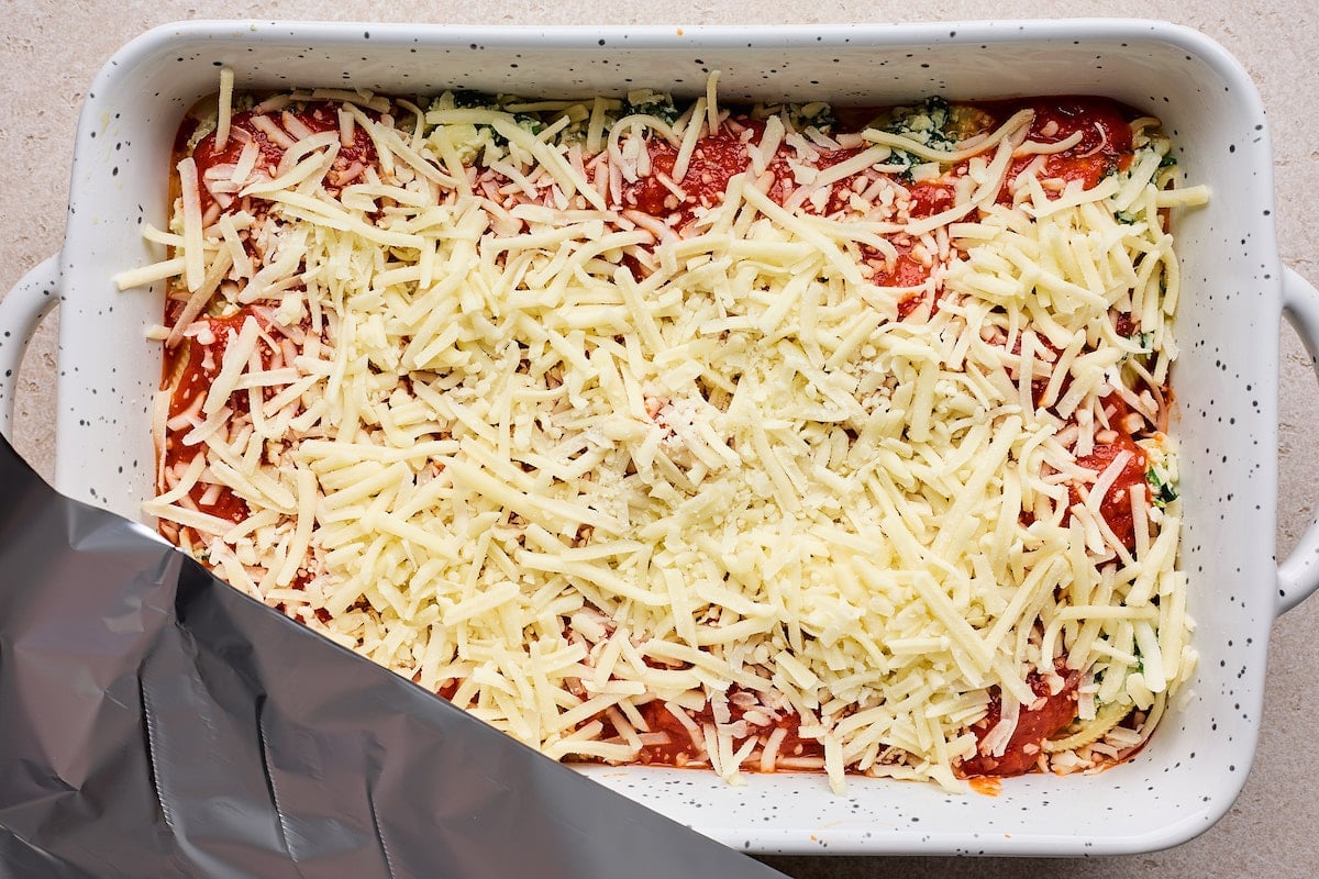 stuffed shells covered in marinara sauce and shredded mozzarella cheese in pan getting ready to be baked.