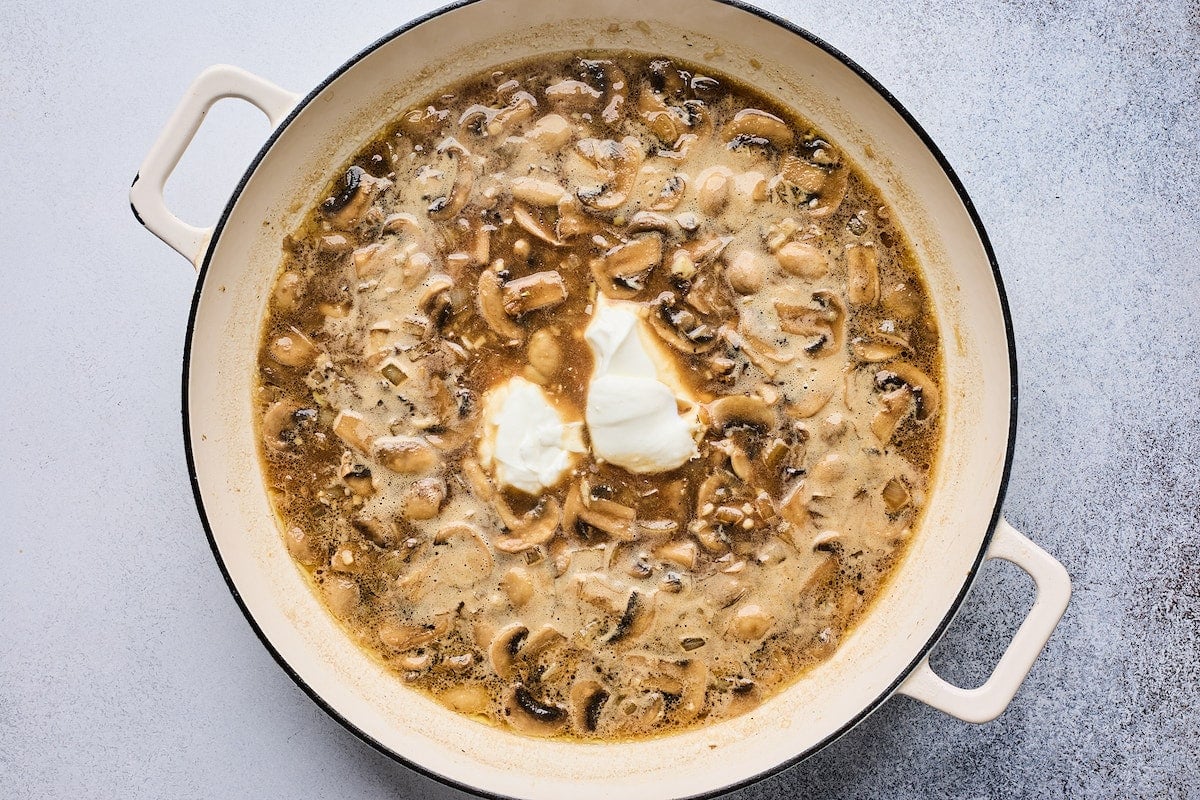 adding sour cream to beef stroganoff sauce in skillet.