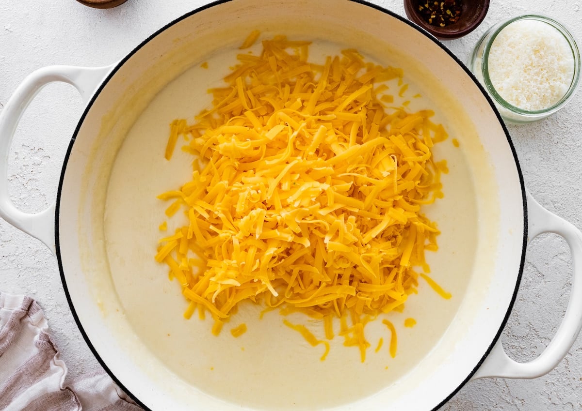 shredded cheese in pot with creamy sauce to make broccoli mac and cheese.