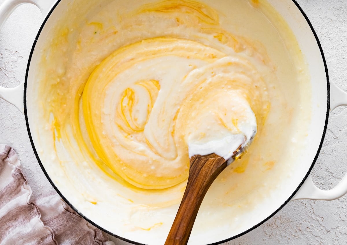 cheese sauce in white pot with wooden spoon to make broccoli mac and cheese.