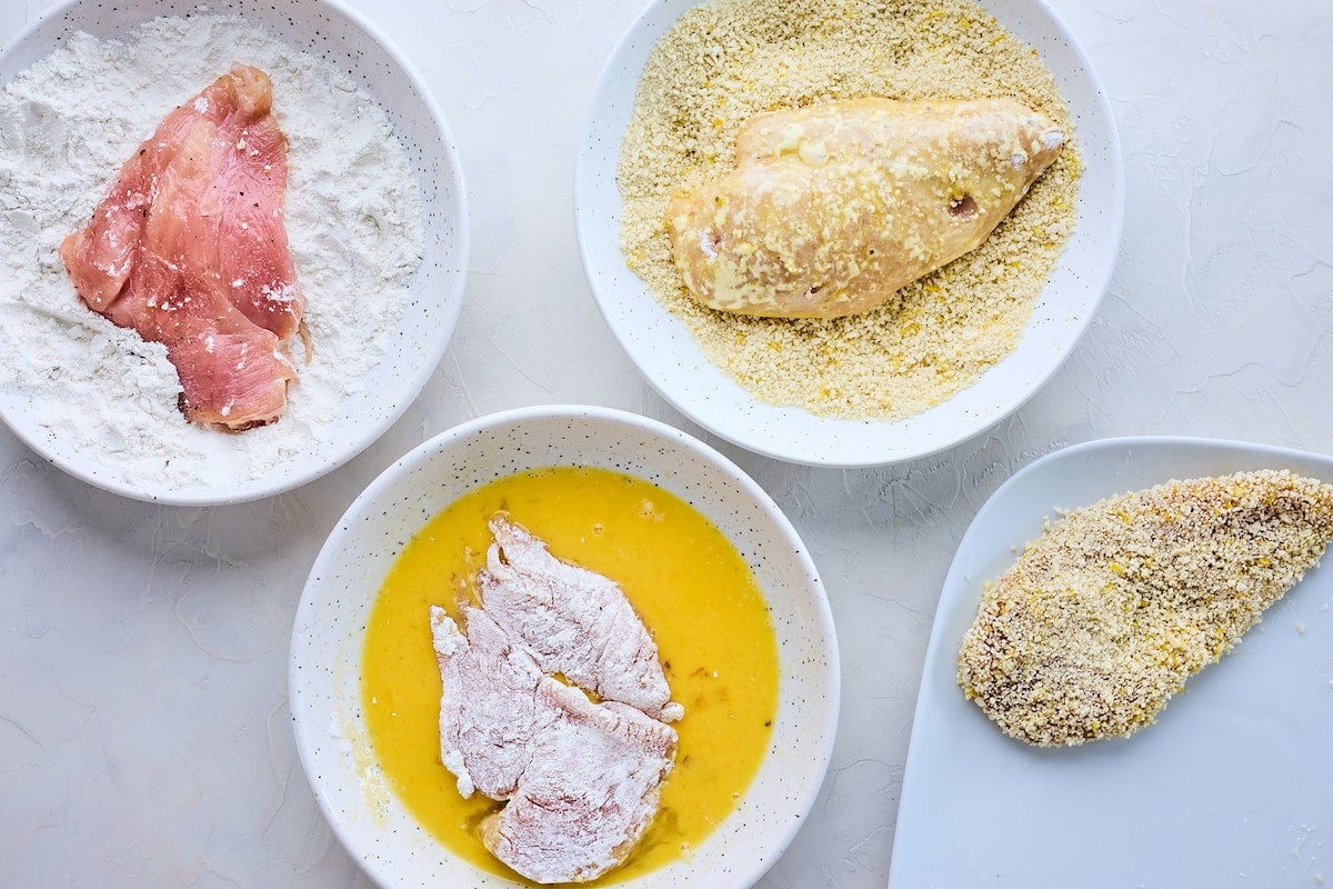 chicken breasts being dredged in egg, flour, and panko to make chicken piccata.