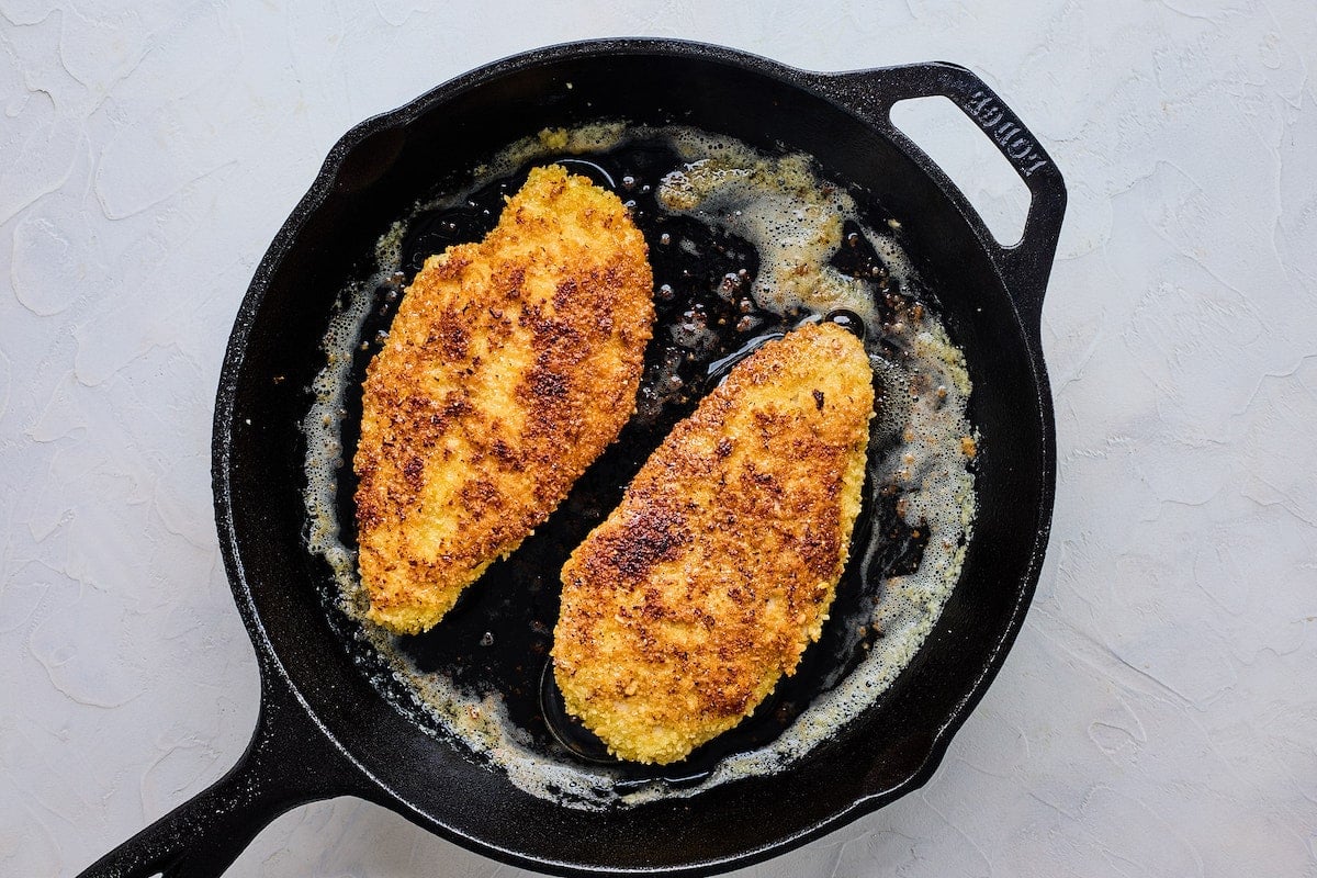 chicken breasts frying in cast iron skillet.
