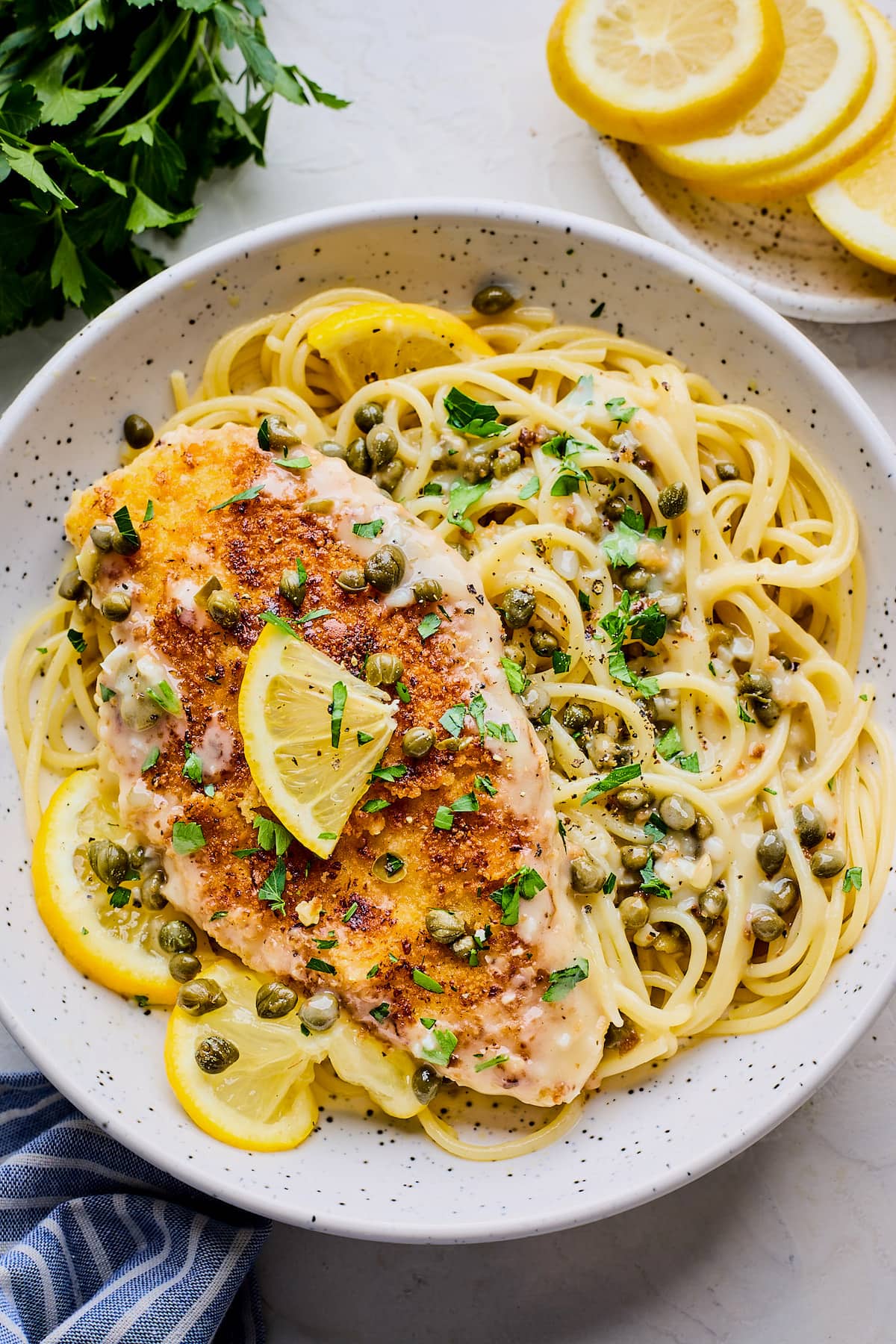 chicken piccata over pasta with capers, lemon, and herbs on plate.