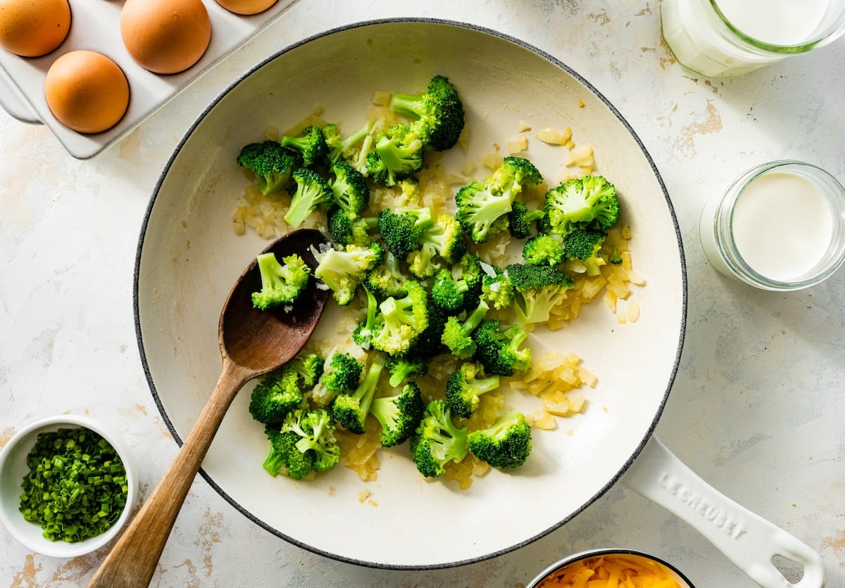 onion and broccoli cooking in skillet with wooden spoon.
