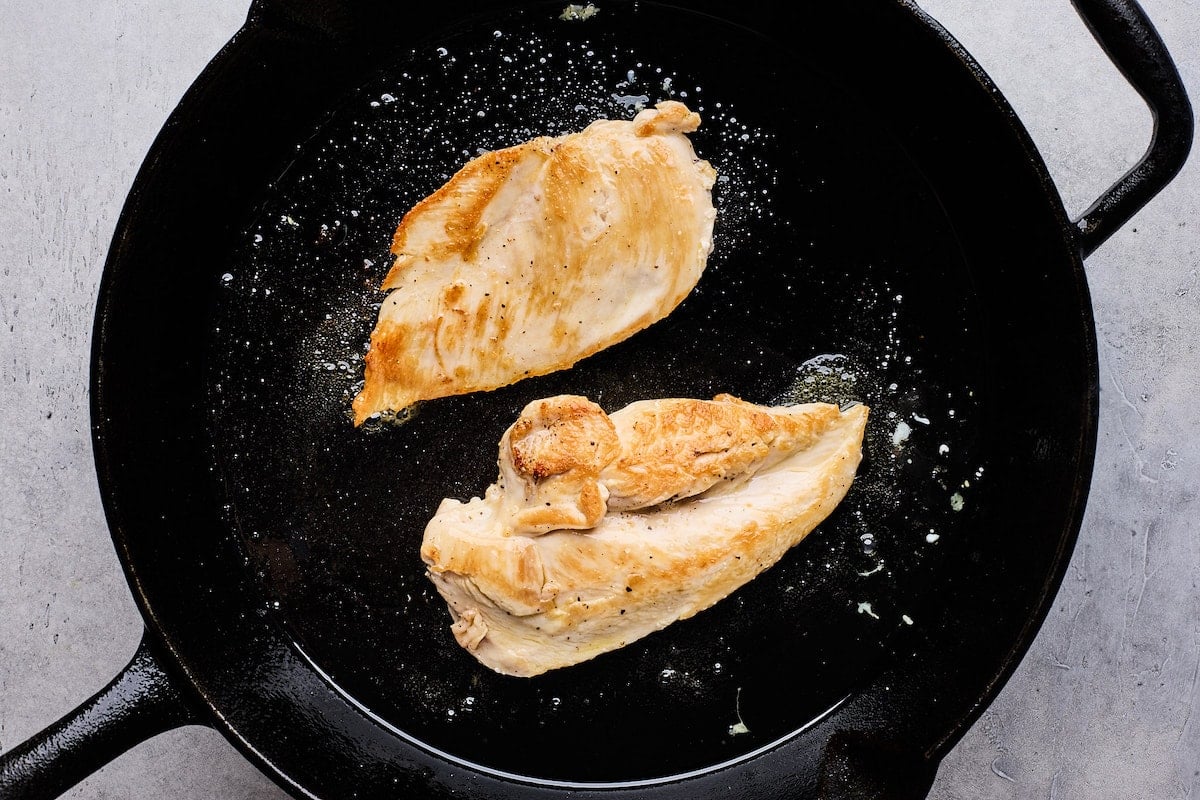 chicken breasts cooking in cast iron skillet.