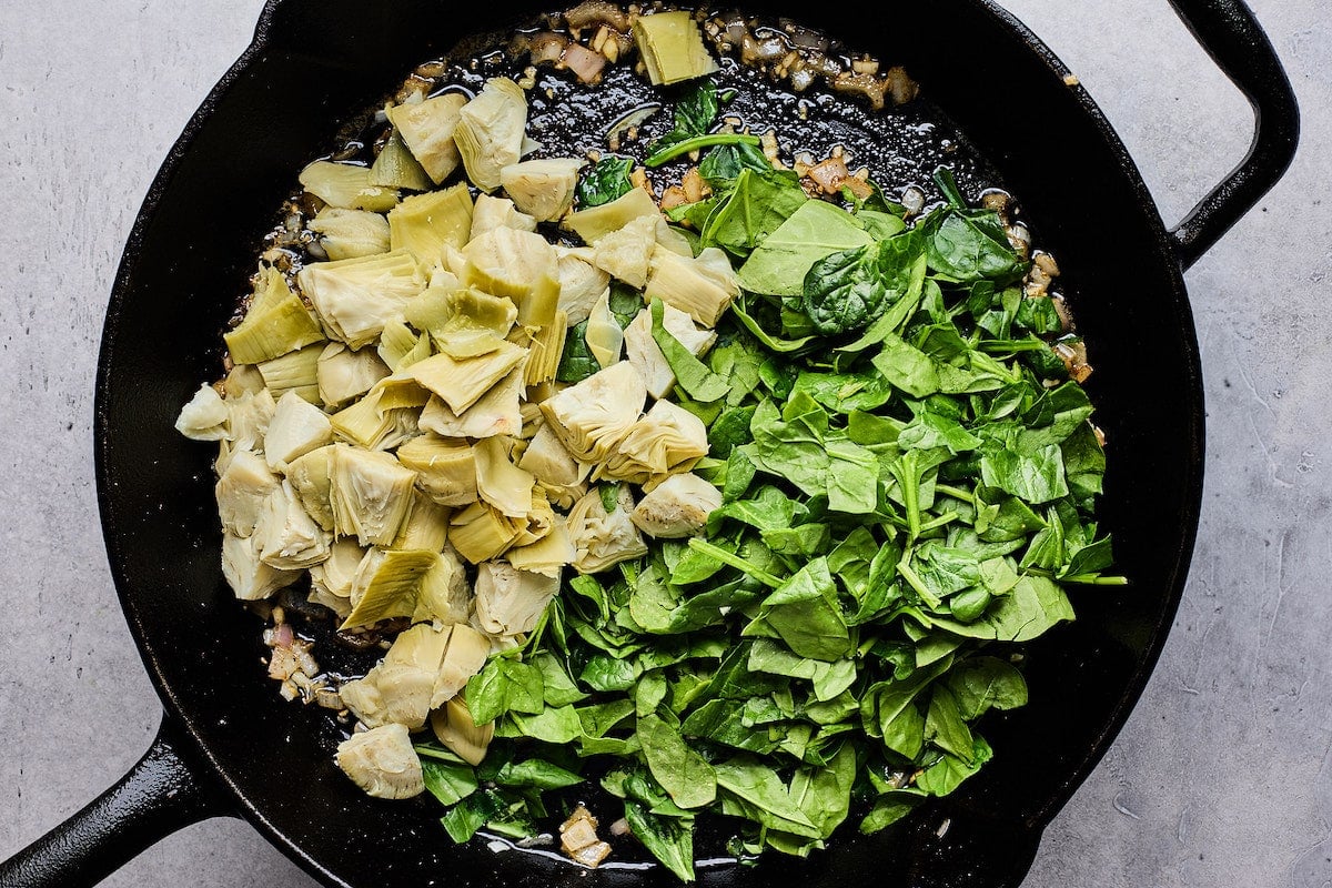shallots, garlic, spinach, and artichoke hearts cooking in cast iron skillet.