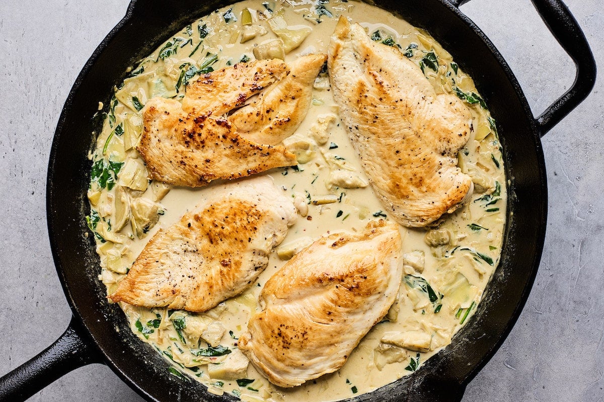 chicken in cast iron skillet with creamy spinach artichoke sauce.
