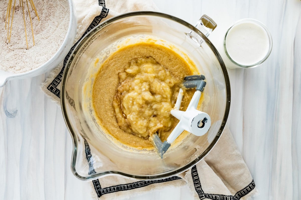 mashed bananas being added to cake batter in mixing bowl.