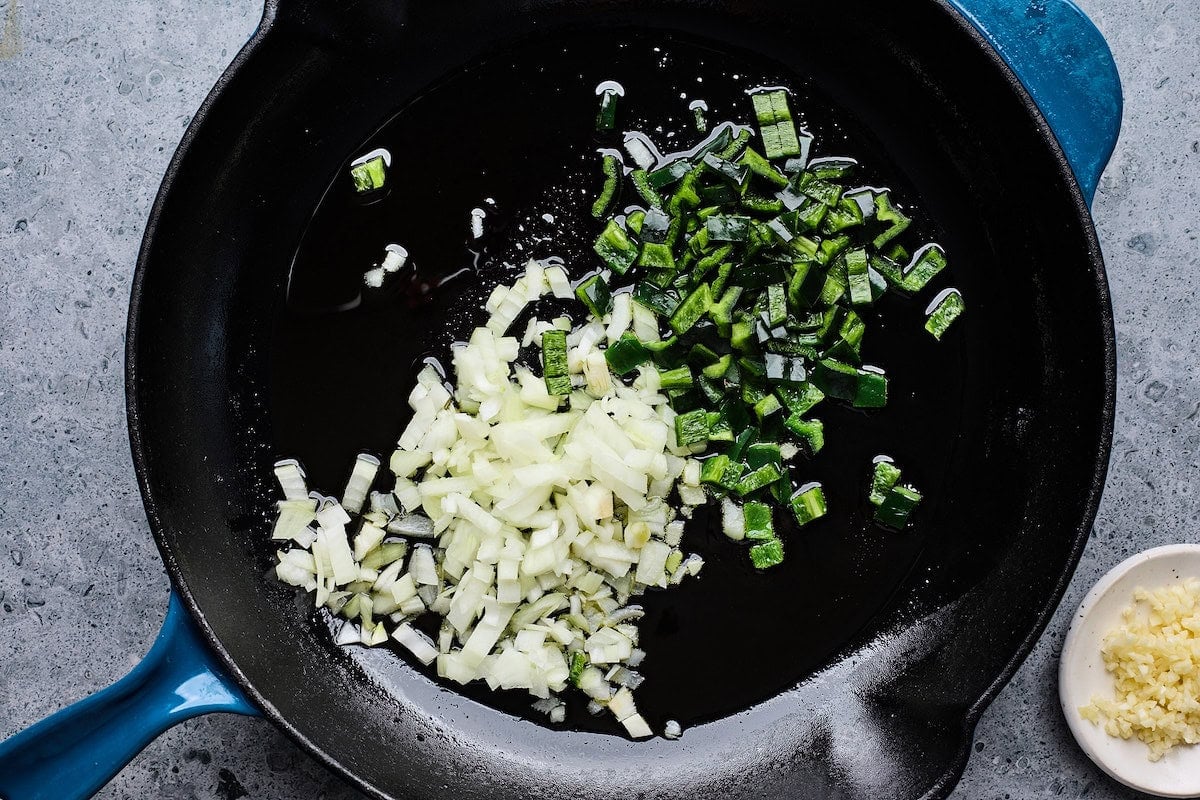 onion and poblano pepper cooking in oil in cast iron skillet.