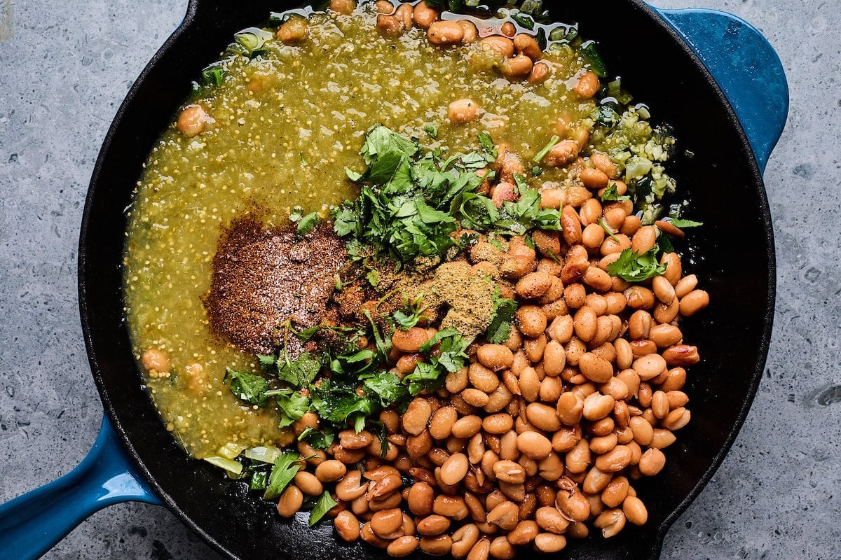 beans, salsa verde, cilantro, and spices cooking in cast iron skillet.