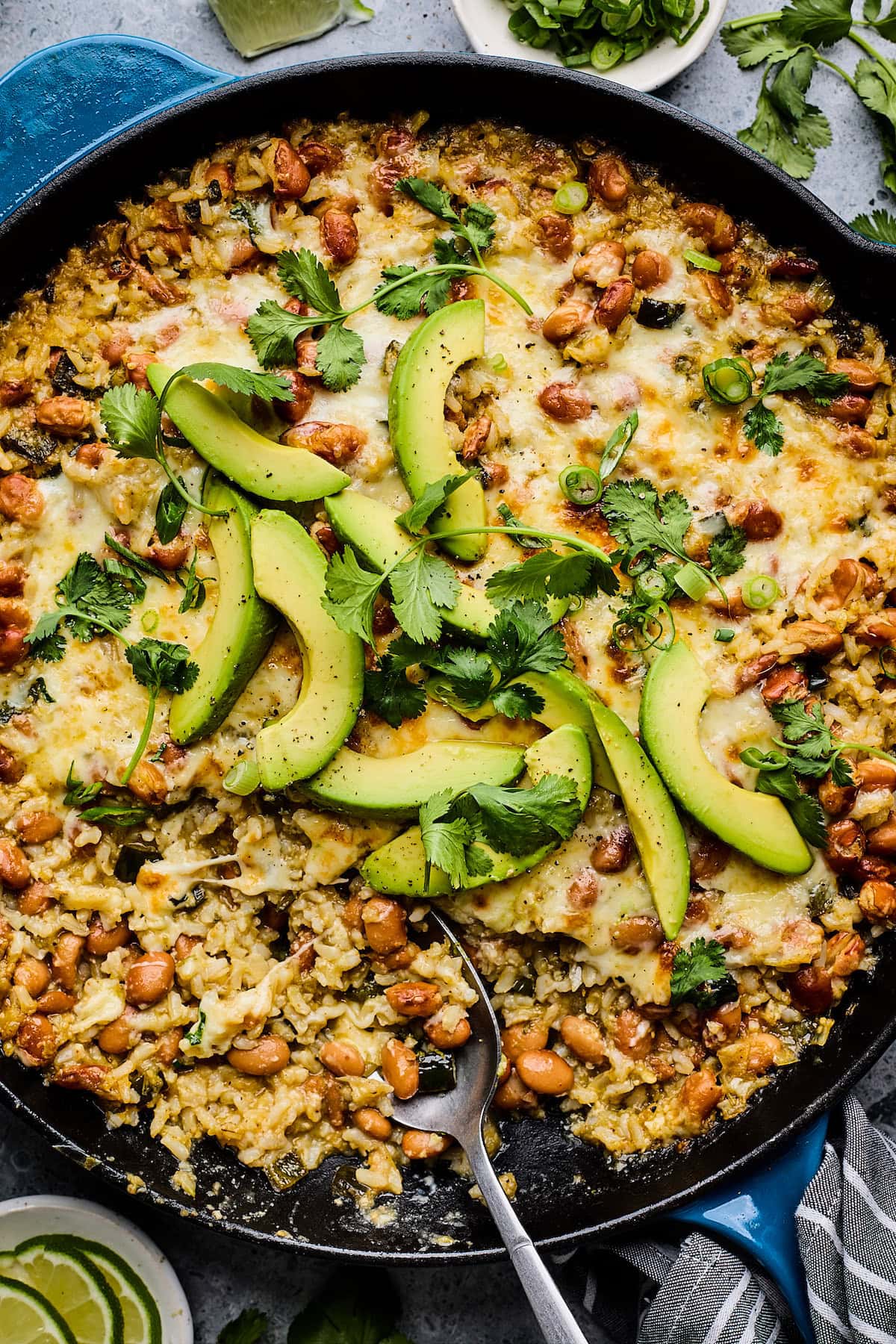 cheesy rice and beans with avocado and cilantro in skillet.