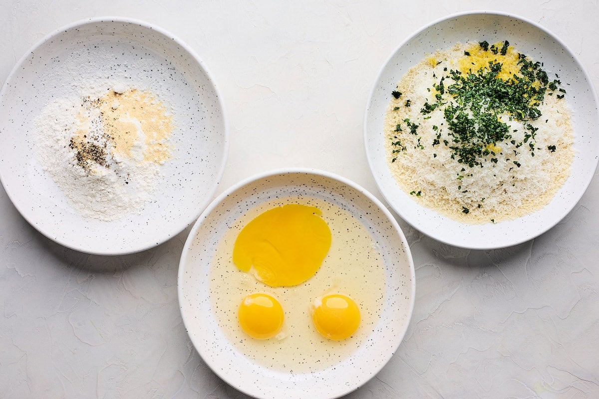 flour and spices in a bowl, eggs in a bowl, and panko bread crumbs and herbs in a bowl to make chicken Milanese.