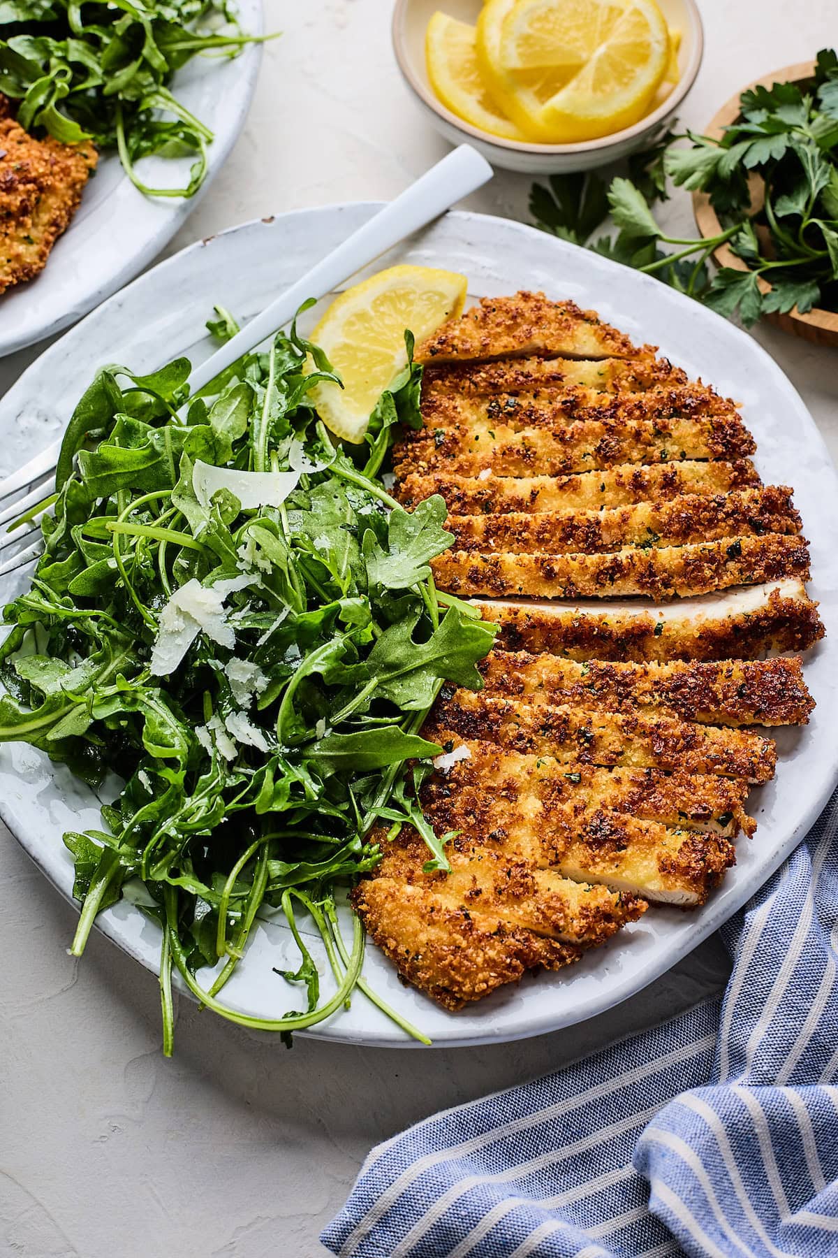 chicken Milanese cut into pieces on plate with arugula salad with Parmesan cheese.