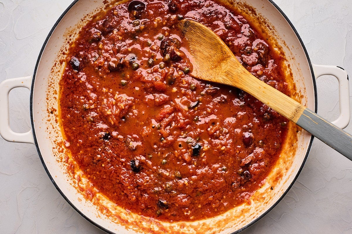 pasta puttanesca sauce in skillet with wooden spoon.
